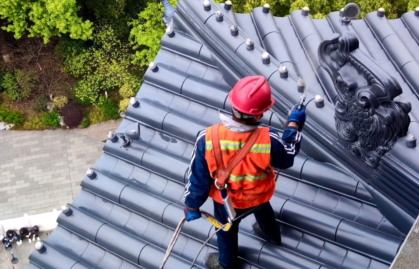 Dachdecker mit Schutzhelm und Warnweste arbeitet gesichert auf einem Ziegeldach