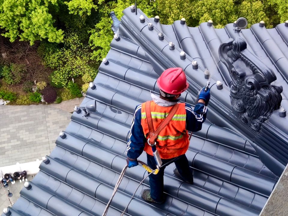 Dachdecker mit Schutzhelm und Warnweste arbeitet gesichert auf einem Ziegeldach