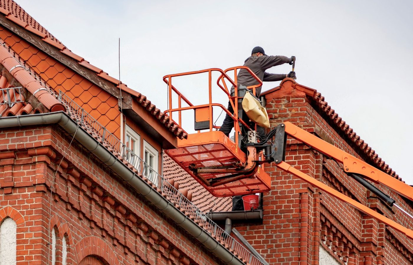 Handwerker arbeitet von einer Hubarbeitsbühne am Dachrand eines Backsteinhauses