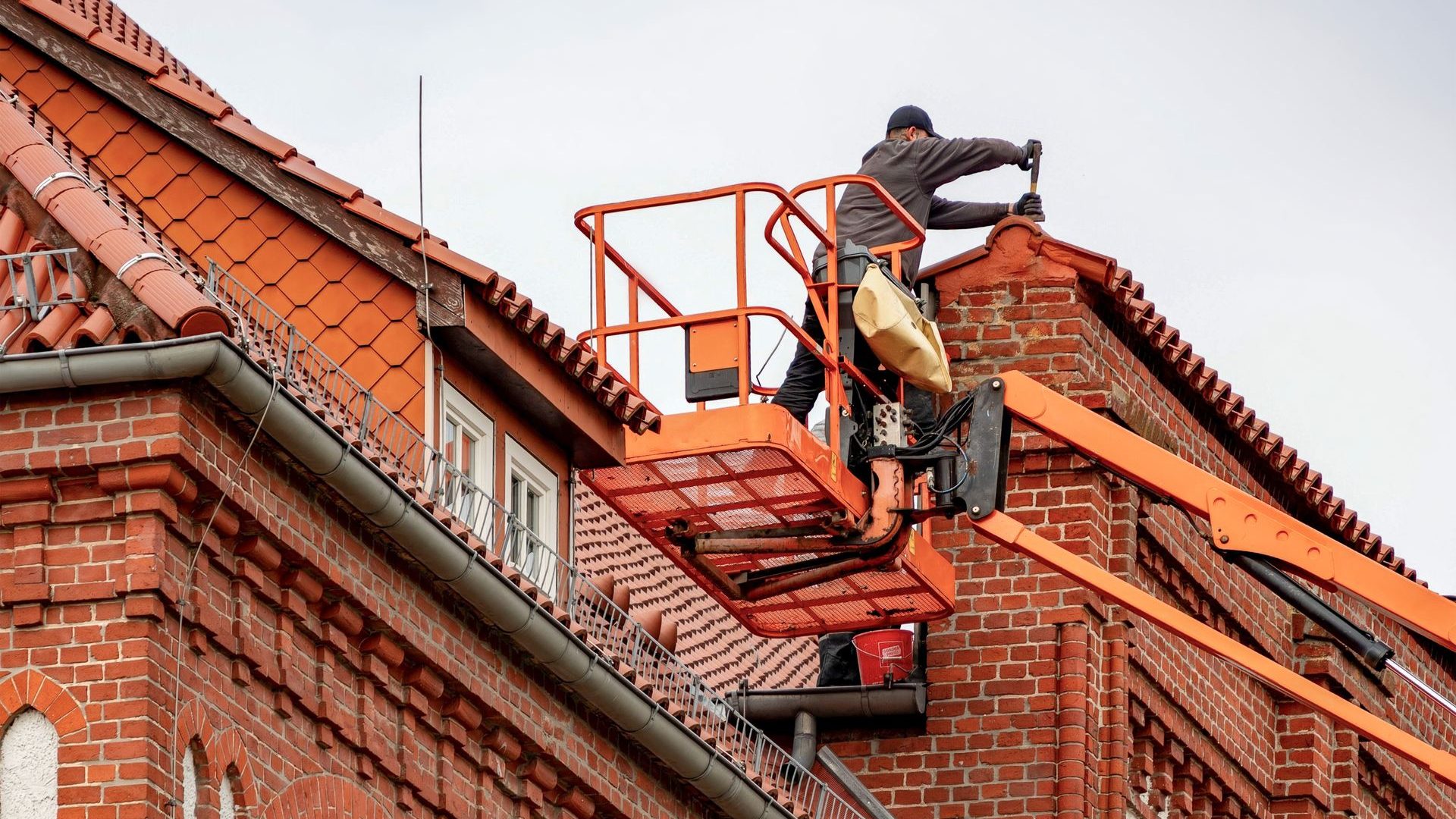 Handwerker arbeitet von einer Hubarbeitsbühne am Dachrand eines Backsteinhauses