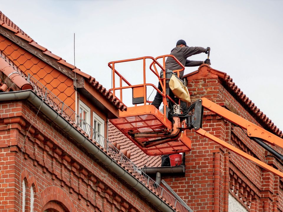 Handwerker arbeitet von einer Hubarbeitsbühne am Dachrand eines Backsteinhauses